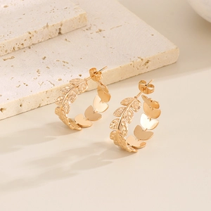 Detailed close-up of golden leaf-shaped C-style titanium steel earrings on stone decor