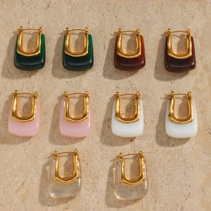 Set of minimalist U-shaped acrylic earrings with gold metal accents on stone background
