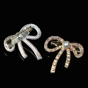 Elegant bow-shaped brooch with inlaid rhinestones and pearl in gold and silver finish