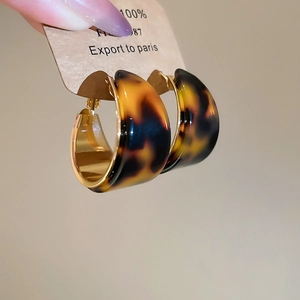 Gros plan de boucles d'oreilles créoles C en résine écaille avec détails dorés à l'or 18K