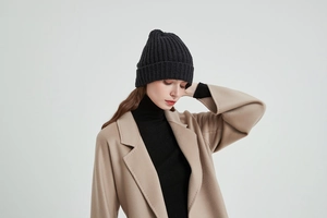 Close-up of black cable knit beanie texture paired with a beige wool overcoat and turtleneck