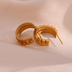 Detail view of 18K gold plated C-shaped earrings with wavy gear texture on silk fabric