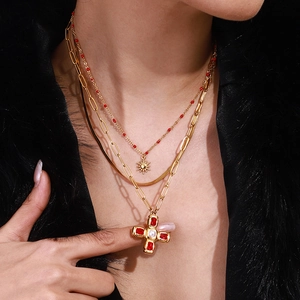 Détail d'un collier multi-rangs doré avec perles rouges et pendentifs soleil et croix