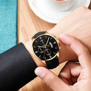 Close-up of a men's quartz watch with gold round dial and black leather strap on wrist