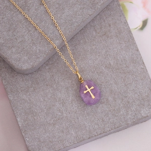 Detail of a purple natural stone cross necklace on a grey stone surface with floral decor