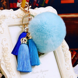 Detail of light blue fluffy pom pom keychain with blue gradient tassels and gold clasp