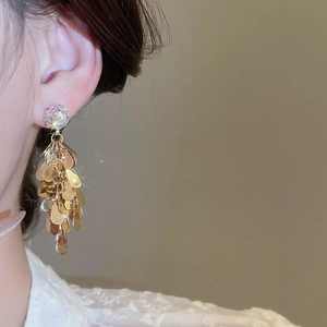 Macro shot of gold sequin tassel earrings with zircon crystal stud on a model