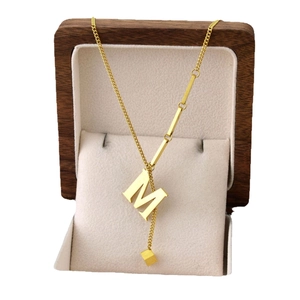 Elegant gold titanium steel necklace featuring M letter and square pendants on a gift pillow