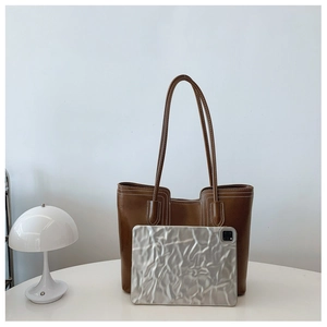 Detail shot of large brown leather tote bag on table showing size compared to a tablet