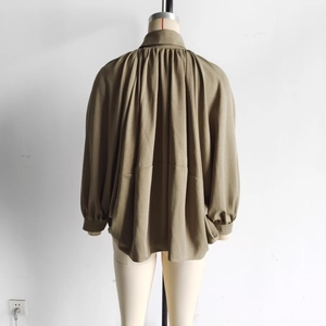 Detail of olive green jacket showing extensive pleated back design on a mannequin