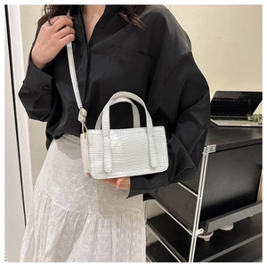 White faux crocodile skin handbag shown on model in a minimalist office setting