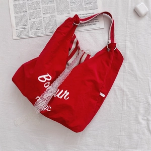 Détail du sac hobo en toile rouge avec lettrage Bonjour blanc et bordure en dentelle