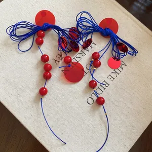 Handmade woven earrings with blue knots and red acrylic sequins on a book cover