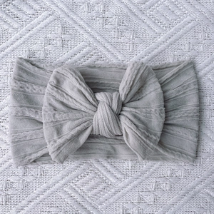 Detail of grey knitted baby headband featuring ribbed texture and large soft bow