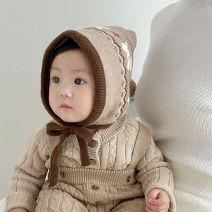 Close-up of knit baby romper and hat set showing soft cable texture and wooden buttons