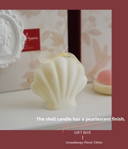 Close-up of pearlized shell-shaped scented candle with silk ribbon and vintage decor