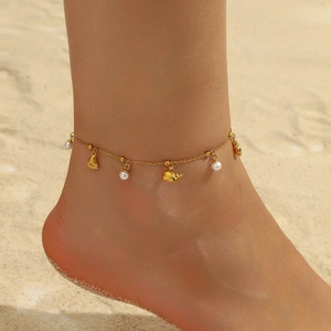 Gold anklet with whale and paw charms with white pearls shown on a sandy beach