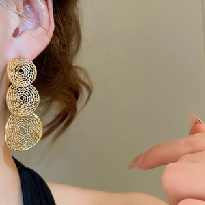 Detail of gold geometric hollow drop earrings with fine textured mesh on a model
