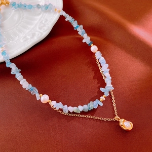 Detail of layered gold necklace with blue aquamarine stones and freshwater pearl pendant