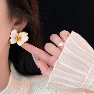 Close-up of a white vintage floral earring with golden details worn by a model