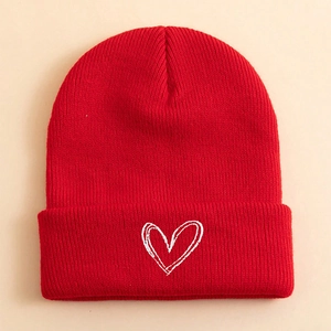 Detailed view of red ribbed knit beanie featuring white heart embroidery on the folded cuff