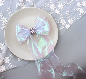 Detail of purple iridescent organza bow hair clip with central rhinestone on a plate
