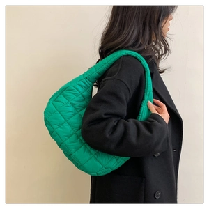 Side view of green quilted down-cotton shoulder bag worn by model in minimalist indoor setting