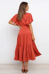 Detalle de vestido largo naranja con cuello en V, mangas con volantes y falda a capas