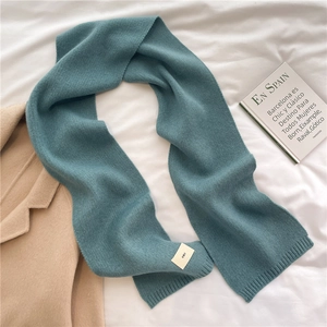 Detailed texture of a dark cyan knitted winter scarf with a small emo fabric label