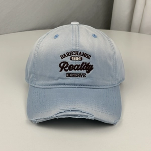 Detailed view of a light blue distressed baseball cap with Reality embroidery on it.