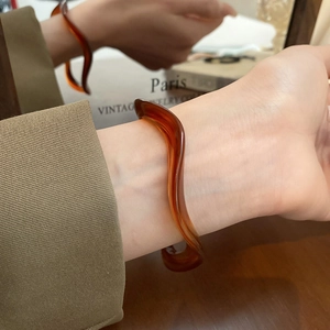 Close-up of wavy amber resin bracelet on a model hand with vintage book background