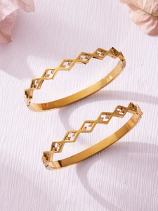 Macro detail of gold geometric bangles with cutout patterns and small inset crystals