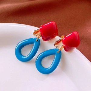 Close-up of red square and blue teardrop earrings on white ceramic plate