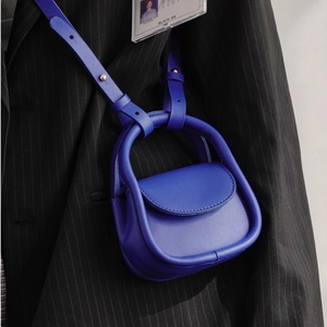 Mini sac à bandoulière en cuir bleu porté sur un costume sombre à rayures fines
