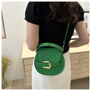 Green leather crossbody bag with round body and gold buckle shown on a model