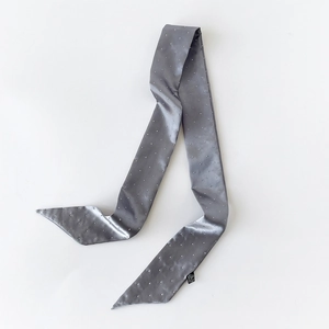 Detail eines grauen Satin-Twilly-Schals mit silbernen Nieten und spitz zulaufenden Enden