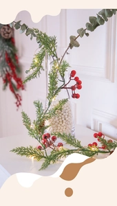 Close-up of Christmas garland with pine needles, red berries, and warm LED lights on a vase