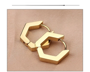 Macro detail of geometric hexagonal gold hoop earrings on beige textured fabric
