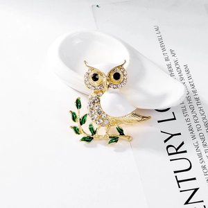 Détail de broche hibou en émail blanc et strass scintillants sur branche dorée