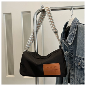 Detail of black nylon crossbody bag with geometric wide strap on a metal display stand
