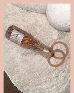 Detailed view of champagne gold rhinestone wine bag with pink circular handles on plush rug