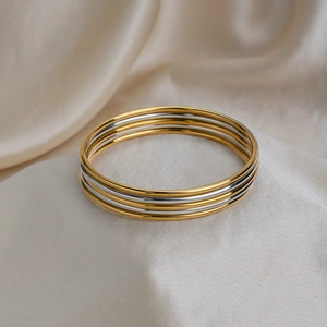 Three-piece layered 60mm stainless steel bangles in gold and silver finish on silk fabric
