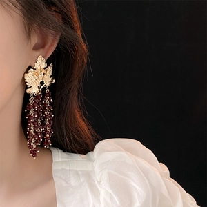 Detail of vintage gold leaf earrings with dark red bead tassels on a model