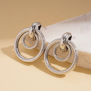 Detail shot of silver geometric double hoop earrings on white textured stone surface