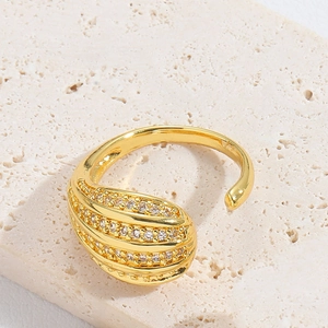 Detail of a golden water-drop shaped ring with sparkling pavé crystals on a stone surface