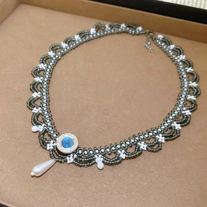 Close-up of woven beaded necklace featuring a blue gemstone and teardrop pearl pendant