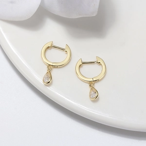 Detail of gold-plated drop earrings featuring pear-cut clear zircon on a white surface