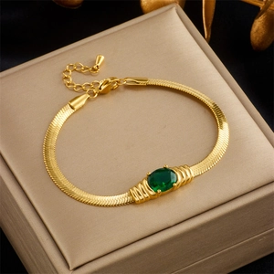 Detail of gold snake chain bracelet with green oval gemstone on a premium jewelry box