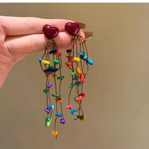 Detailed view of colorful shell tassel heart earrings held to show texture and length