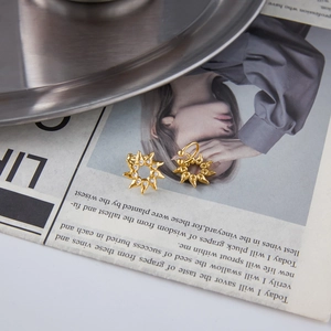 Macro view of gold sun-shaped stud and clip-on earrings with zircon on a vintage paper